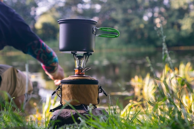 Toeristisch fornuisgas voor kamperen en recreatie tegen de achtergrond van de natuur en het meer Een man kookt buiten eten