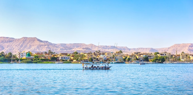 Toeristische boot drijvend langs het dorp op de rivier de Nijl in Luxor, Egypte