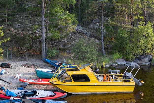 Toeristische kajaks en een gele boot in een rotsachtige en beboste baai van het meer Apparatuur is verspreid over de boten aan de kust