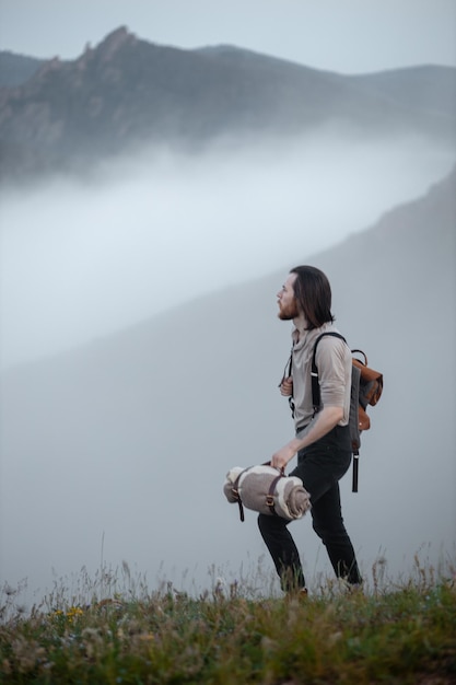 Toeristische reiziger hipster gekleed in vintage stijl met rugzak en plaid tegen de achtergrond van bergen in mist