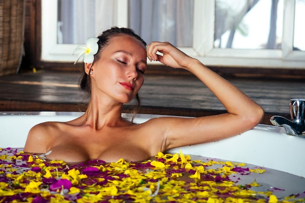 Toeristische sexy meisje nemen van een bad met tropische bloemen op vakantie in een exotische zomer country jonge mooie vrouw in ronde jacuzzi eco hotel spa salon ontspannende aromatherapie en massage Vrouwendag