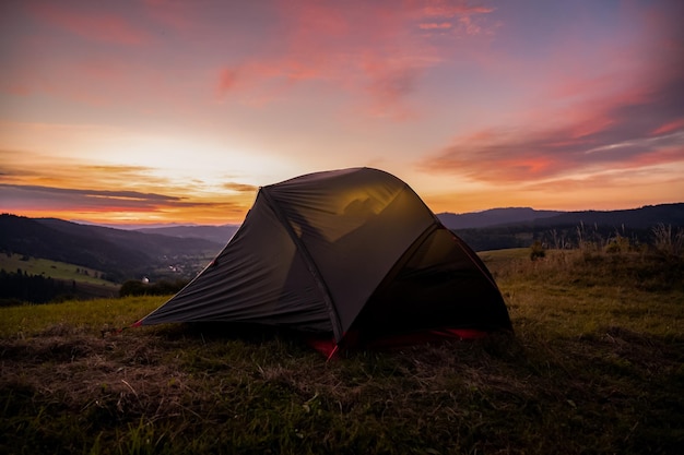 Toeristische tent in de bergen onder dramatische avondlucht Kleurrijke zonsondergang in bergen Camping travell concept Reizigersmensen die genieten van de alternatieve vakantie van het advanture