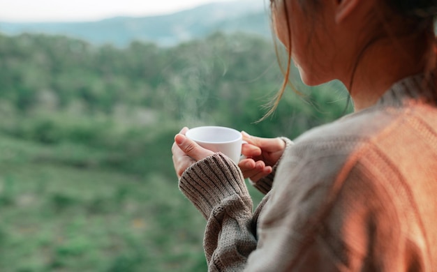 Toeristische vrouw drinkt een warme drank uit een kopje en geniet van het landschap in de bergen