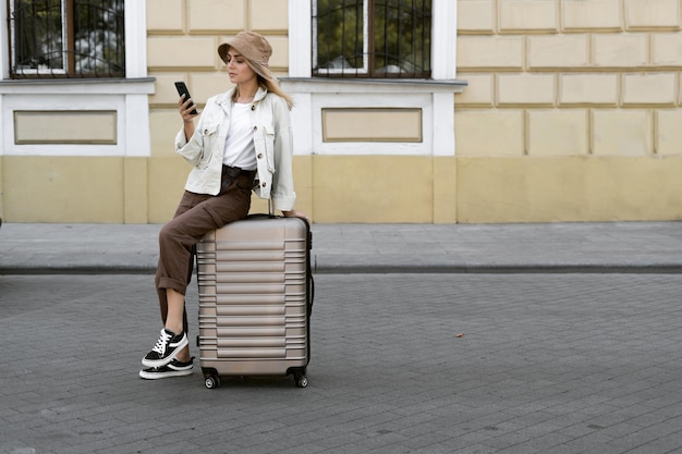 Toeristische vrouw in een Europese stad, toerisme in Europa. een jong meisje gekleed in een panama zit op een grote koffer en leest een chat in een smartphone. Roamen. Ruimte kopiëren