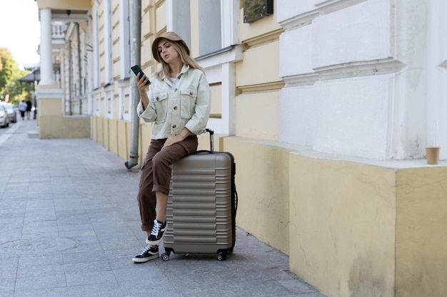 Toeristische vrouw in een Europese stad, toerisme in Europa. Zit op een grote koffer op de stoep aan de telefoon te typen.