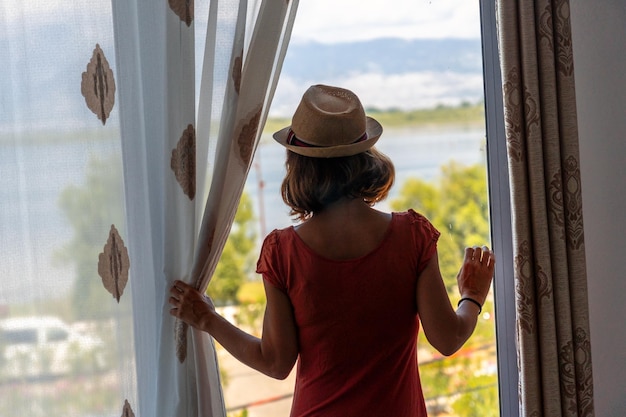 Toeristische vrouw kijkend naar uitzicht vanuit hotelraam tijdens zomervakantie reizen levensstijl concept