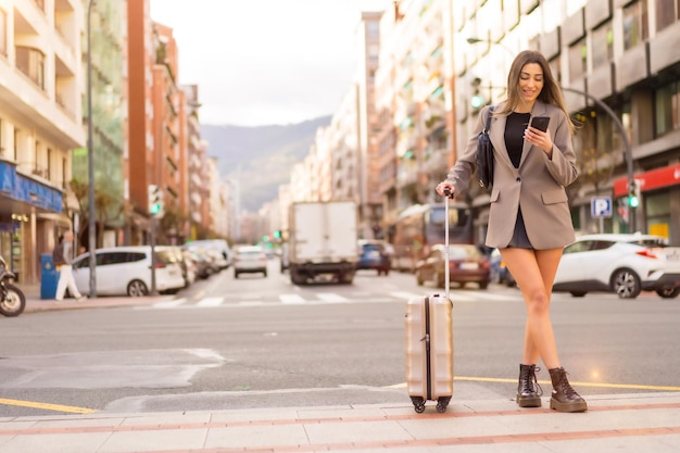 Toeristische vrouw met koffer in de stad concept vakanties levensstijl kijken naar de telefoon