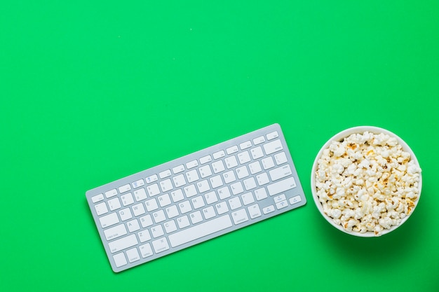 Toetsenbord en kom met popcorn op een groene achtergrond. het concept van films, tv-shows, shows, online sporten. plat lag, bovenaanzicht