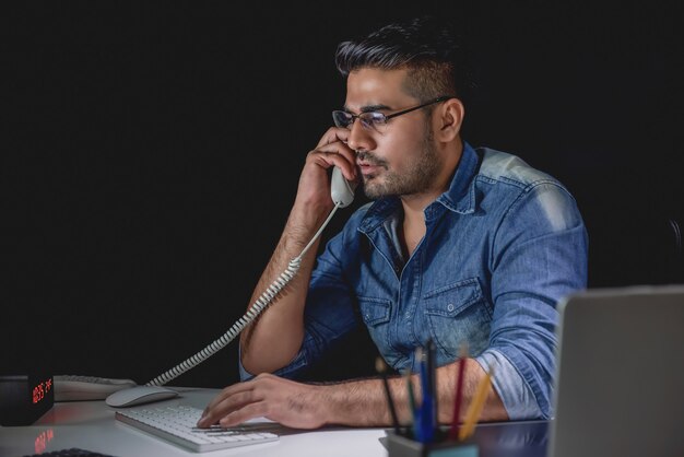Toevallige Aziatische zakenman die telefoongesprek bij nacht in het bureau beantwoordt