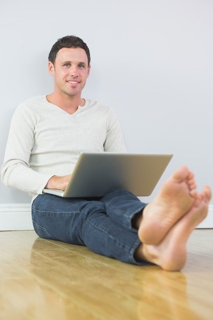 Toevallige gelukkige mens die tegen muur leunt die laptop met behulp van