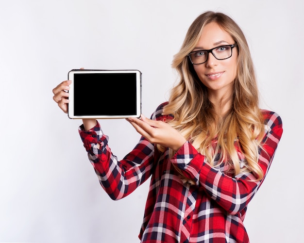 Toevallige glimlachende vrouw die het lege scherm van de tabletcomputer over grijze achtergrond tonen.