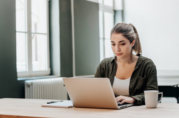 Toevallige jonge vrouw die laptop thuis bureau met behulp van.