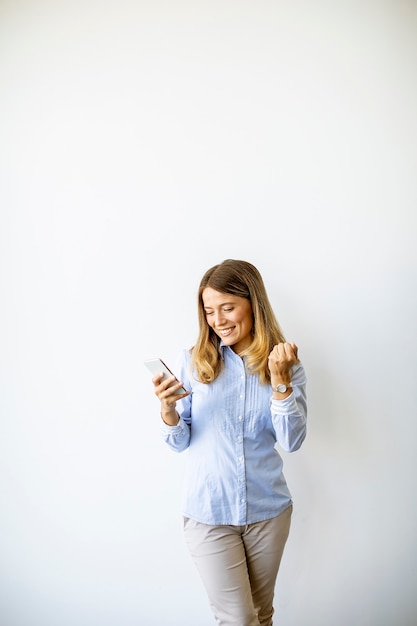 Toevallige vrij jonge bedrijfsvrouw die zich door de muur in het bureau bevindt en mobiele telefoon met behulp van