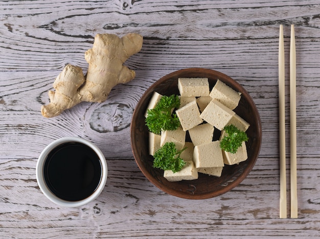 Сыр тофу в глиняной миске с корнем имбиря на деревянном столе. соевый сыр. вегетарианский продукт. плоская планировка.