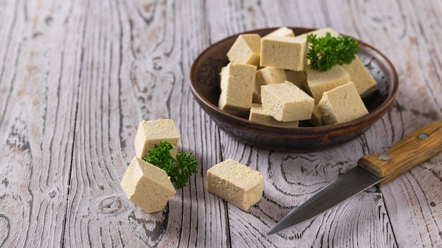 Tofu kaas in een kom van klei en een mes op een houten oppervlak. Soja kaas. Vegetarisch product.