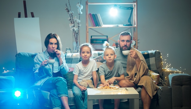 Единение Счастливая семья смотрит через проектор телевизионные фильмы с попкорном и напитками