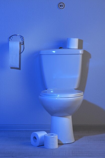 Туалетная миска и туалетная бумага в ванной с синим светом
