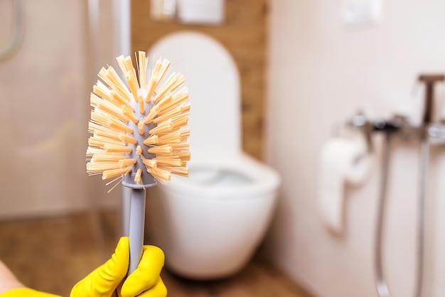 Toilet brush in hand in a yellow glove closeup Bathroom and toilet background