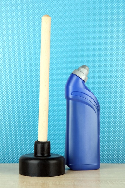 Toilet plunger and cleaner bottle on blue background