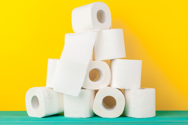 Toiletpapierbroodjes die tegen gele achtergrond worden gestapeld