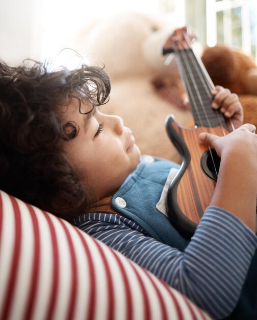 Tokkelen voor dromen Shot van een schattige jongen die thuis met een gitaar speelt in zijn slaapkamer