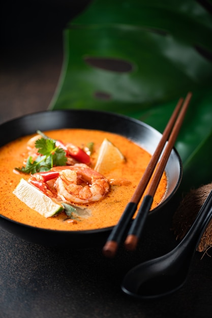 Tom yam kung spicy thai soup with shrimp in a black bowl on a dark surface, selective focus