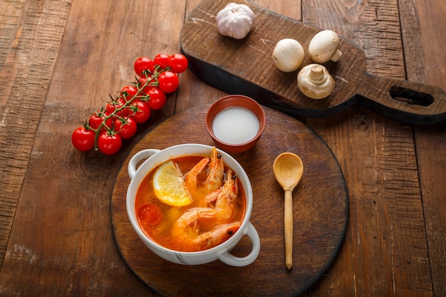 Tom yam soep met garnalen en kokosmelk op tafel op een rond bord naast kokosmelk champignons en tomaten