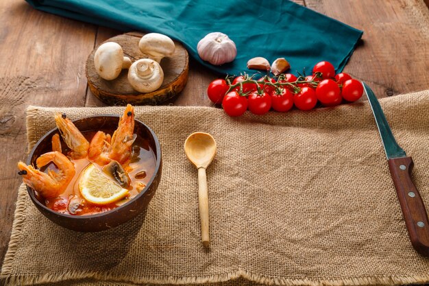 Tom yam soep met garnalen en kokosmelk op tafel op een servet naast de ingrediënten en een houten lepel. ruimte kopiëren. Horizontale foto