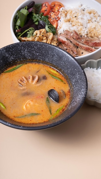Tom yam soup with seafood and bowl with rice veal and vegetables angle view