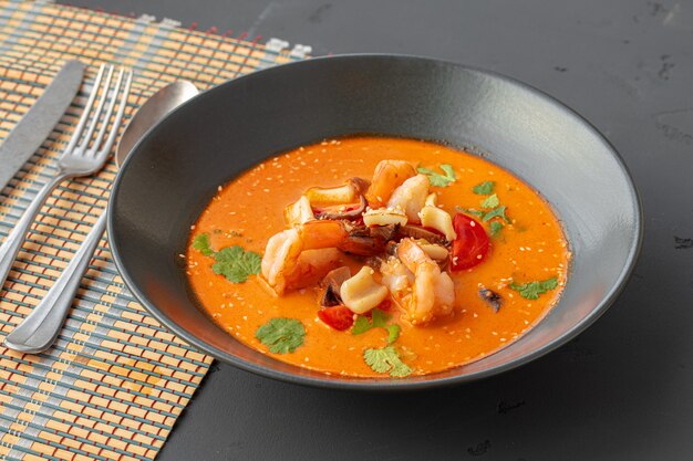 Tom yam thai soup in black bowl on gray table