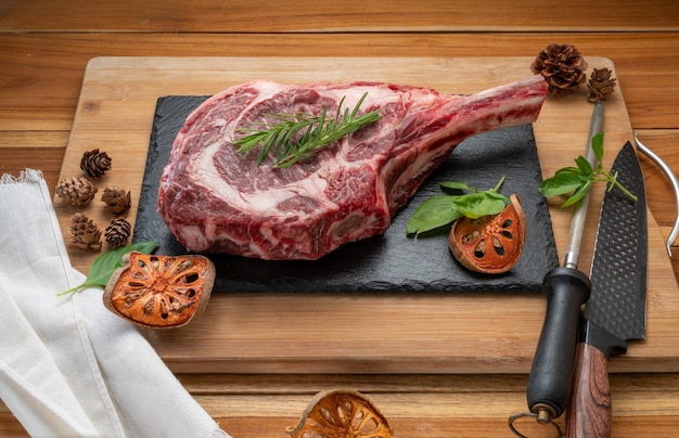 Tomahawk beef steak with rosemary on black plate Fresh Tomahawk beef on wooden background