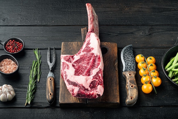 Tomahawk rauwe verse biefstuk met kruiden set, met ingrediënten van de grill, op zwarte houten tafel