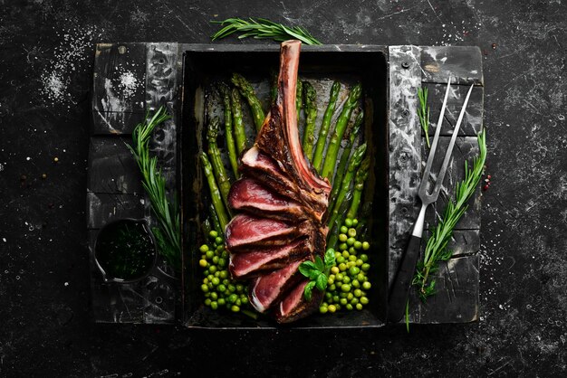 Tomahawk steak on the bone grilled steak with asparagus and\
green peas on a black background top view free copy space