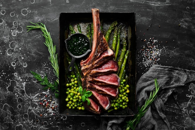 Tomahawk steak op het bot Gegrilde steak met asperges en groene erwten Op een zwarte achtergrond Bovenaanzicht Gratis kopieerruimte