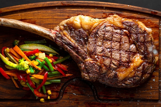 Photo tomahawk steak and veggies on a serving board. low key image, horizontal orientation