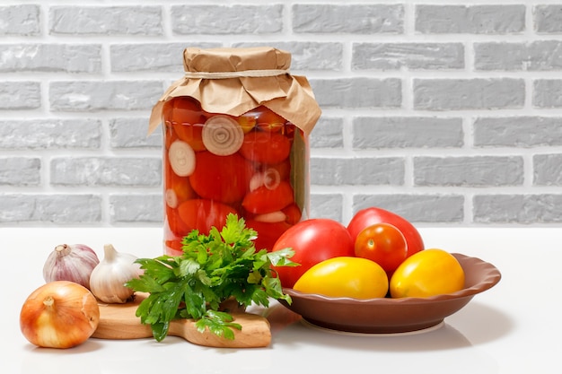 Tomaten bewaard in een glazen pot, verse tomaten, peterseliebladeren, knoflook, een ui op de keukentafel.