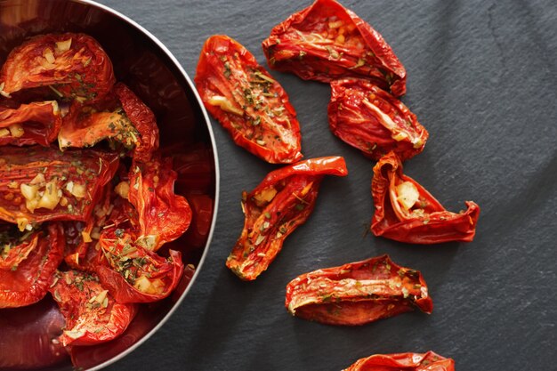 Tomaten die in reepjes in de zon worden gedroogd die in metaalschotel liggen op donkere achtergrond