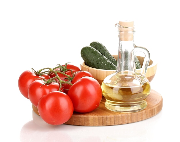 Tomaten en komkommers met olie op een houten bord op wit wordt geïsoleerd