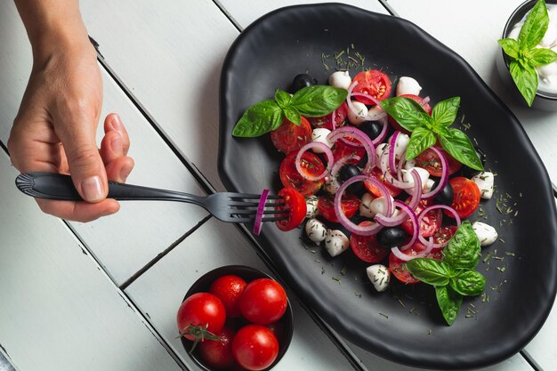 Foto tomaten en mozzarella caprese salade en pesto saus met olijven op witte tafel geserveerd met vork