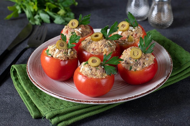 Tomaten gevuld met tonijn en olijven op een rond bord op een donkergrijze achtergrond