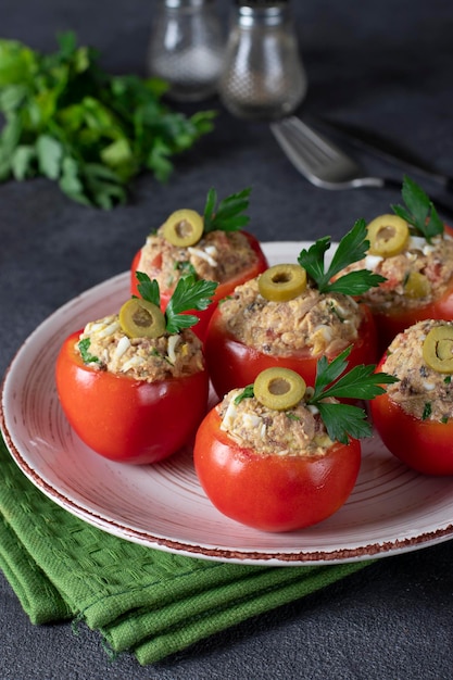 Tomaten gevuld met tonijn en olijven op een ronde plaat op een donkergrijze achtergrond. Verticaal formaat