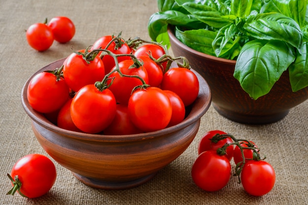 Tomaten in kom met basilicum op stoffenachtergrond