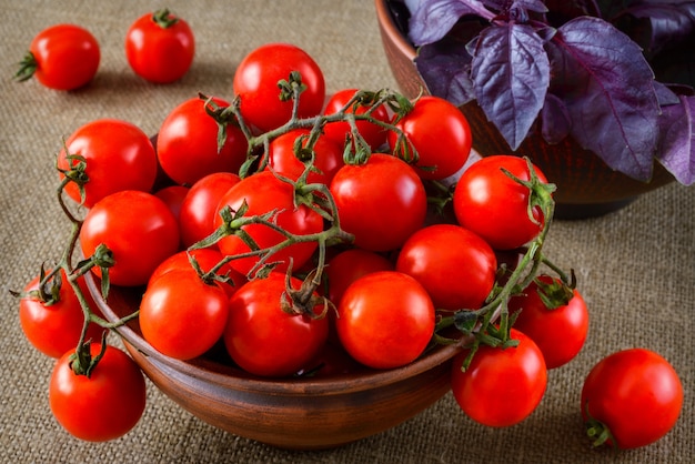 Tomaten in kom met basilicum op stoffenachtergrond