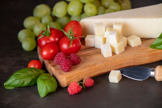 tomaten, kaas, basilicum, frambozen en druiven op een olijfbord op een donkere achtergrond