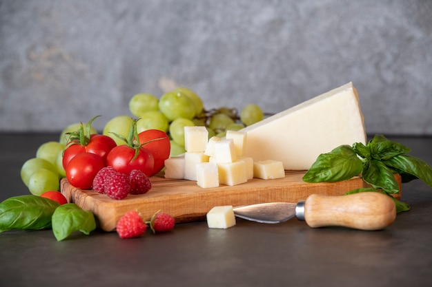 tomaten, kaas, basilicum, frambozen en druiven op een olijfbord op een donkere achtergrond