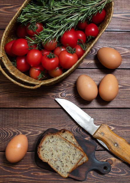 Tomaten komkommers een paar takjes rozemarijn kippeneieren en gesneden brood op een houten tafel