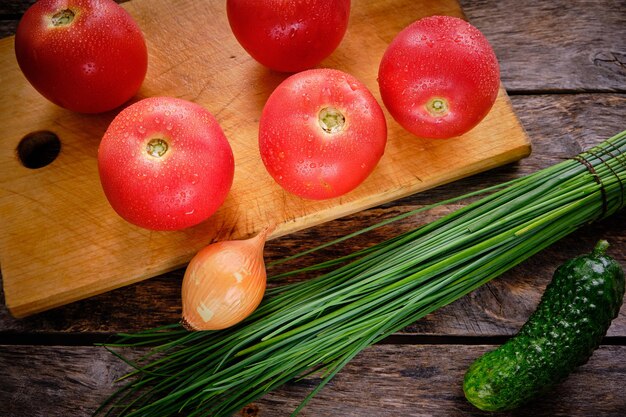 Tomaten op een snijplank, groene uien en komkommer op een oude houten tafel.