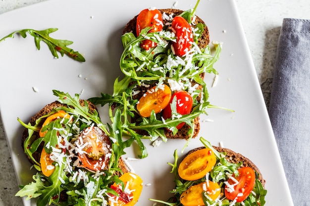 Foto tomaten, rucola en kaas sandwiches op een grijze plaat, bovenaanzicht.