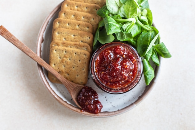 Tomatenjam confiture of saus met crackers en groene blaadjes salade Bijzondere hartige jam