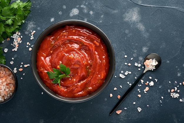 tomatenketchup pikante saus in een zwarte kom met kruiden en verse tomaten